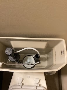 Top-down view of an open toilet tank showing the inner plumbing mechanisms, including the fill valve, flapper, and refill tube.