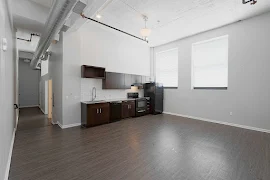 Open concept living and dining room with high ceilings, light walls, kitchen area, large windows, and wood-inspired flooring