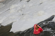 A woman worships the sun god as she stands amid the foam covering the polluted Yamuna river during the Hindu religious festival of Chhath Puja in New Delhi. 