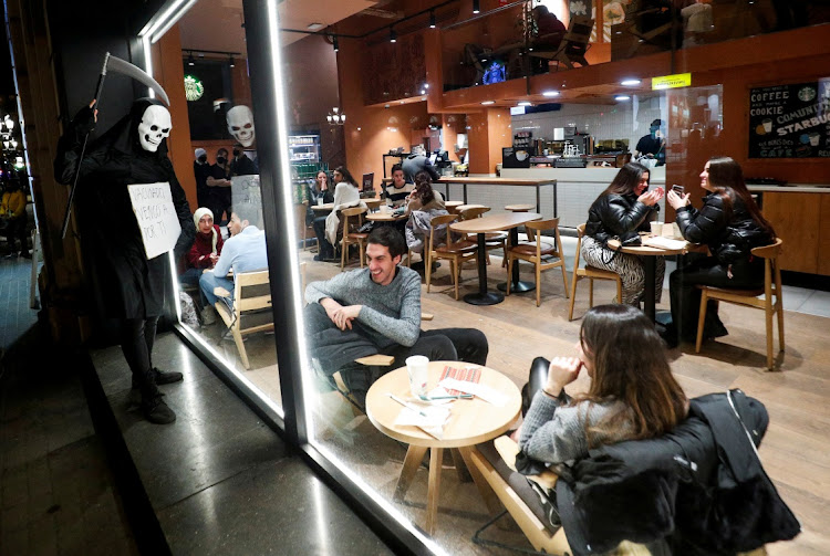 People sitting in a cafe react as a protester wearing a costume and holding a placard reading "Vaccinated, I am coming for you" stands by the window, during a demonstration against the Covid-19 passport restrictions imposed to contain the spread of the coronavirus disease (Covid-19) in Barcelona, Spain, January 22, 2022.