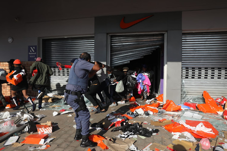 People looting a shop in the Springfield Value Centre in Durban flee from a police officer on July 12 2021 as riots continued under the hashtags #FreeJacobZuma and #KZNShutdown on social media.