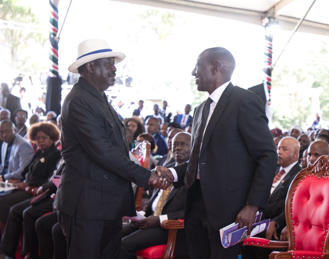 President William Ruto rises to greet Azimio leader Raila Odinga during the funeral of Field Marshal Mukami Kimathi in Nyandarua.