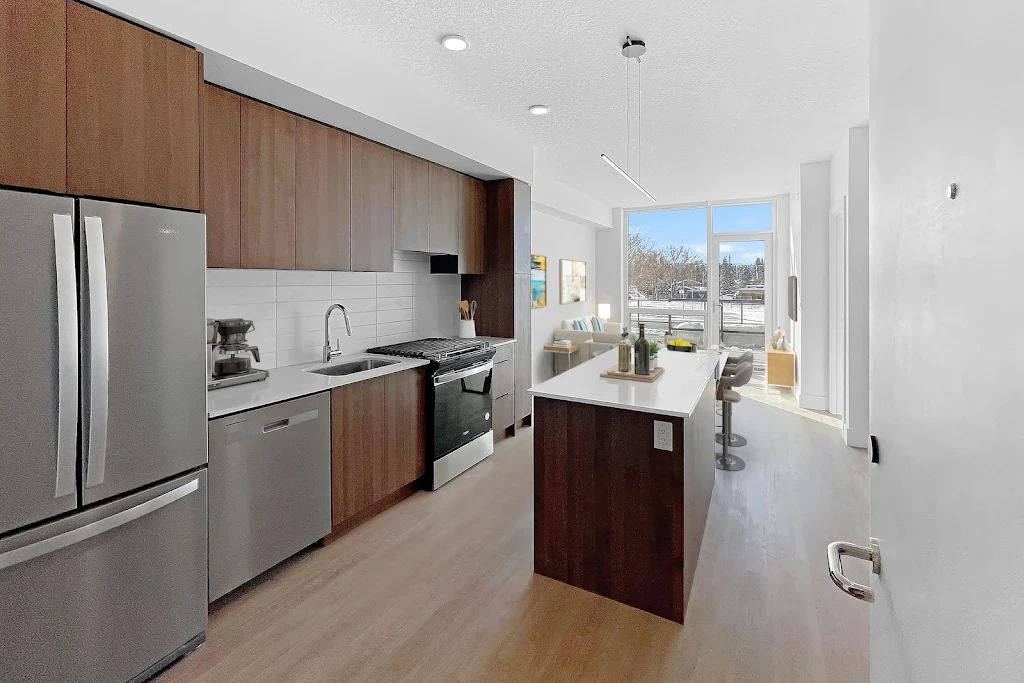 Modern apartment kitchen with stainless steel appliances, wooden cabinets, and bright natural light.