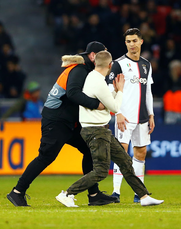 A pitch invader is apprehended by a steward as Juventus' Cristiano Ronaldo looks on