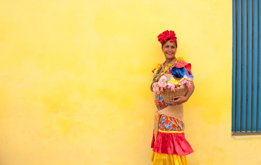 Cuban-Woman-in-Colorful-Dress-in-Front-of-Yellow-Wall.jpg - A flower seller in Old Havana.