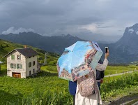 3 mensen onder parasol met foto's maken een kiekje van berglandschap