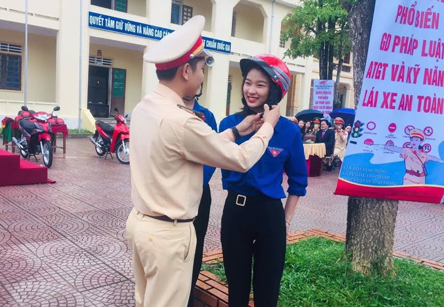 Cán bộ Công an huyện Thanh Chương hướng dẫn học sinh cách đội mũ bảo hiểm đúng quy định