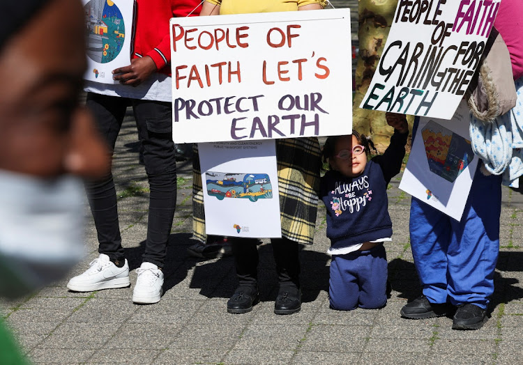 A girl sits near climate activists who hold placards as they call for climate justice resistance against oil and gas corporations and to end fossil fuels outside the Cape Town International Convention Centre during the Southern Africa Oil and Gas Conference in Cape Town, South Africa, September 13, 2023.