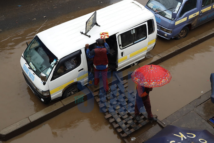 Pedestrians with umbrellas waiting to board vehicles at the Ngara bus stop on December 3, 2019.