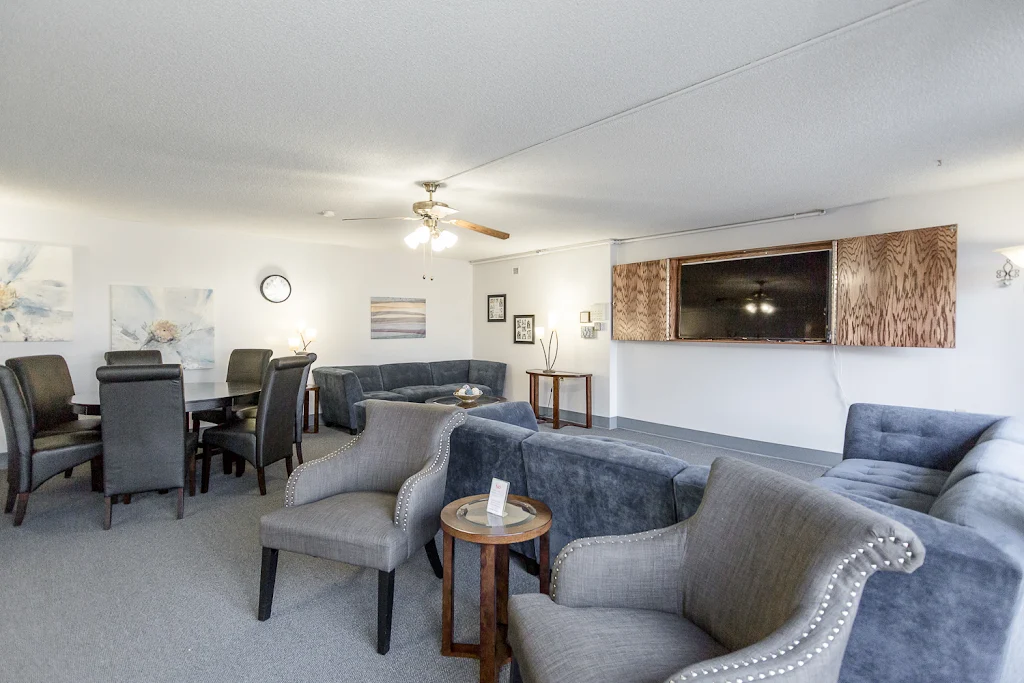 Seating area in Nowlin hall clubhouse including plush sectional and chairs, dining table and chairs, ceiling fan, mounted tv