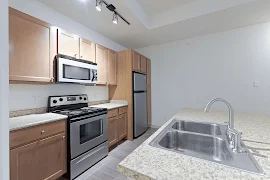 Modern apartment kitchen with stainless steel appliances, wooden cabinets, and granite countertops.