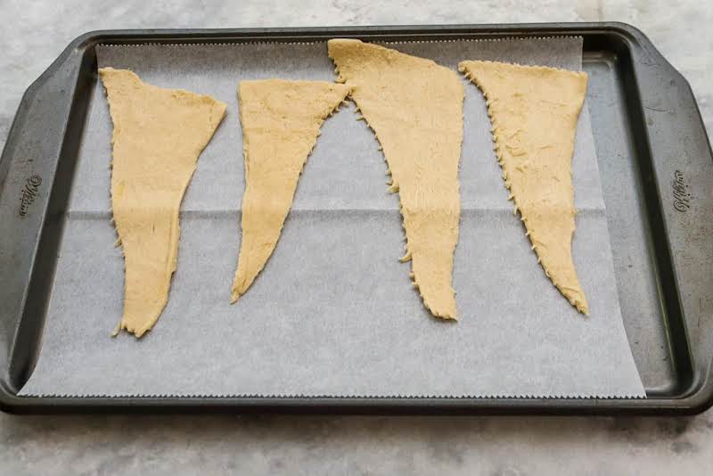 Crescent Roll Dough Unrolled And On A Parchment Paper-lined Baking Sheet.