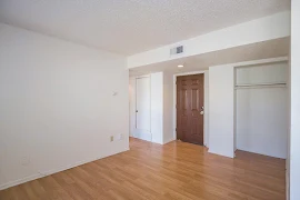 Living area looking at front door and into bedroom entry, featuring white walls, white trim, wood floors, utility closet