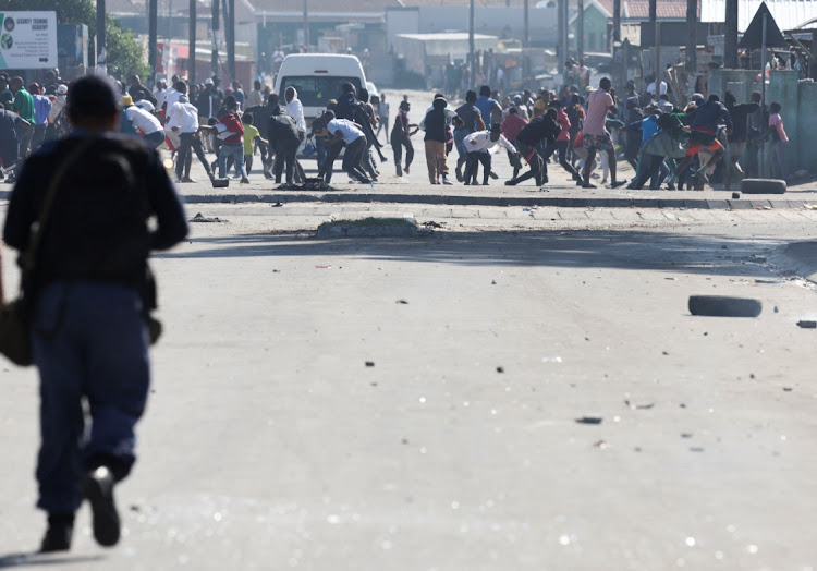 A police officer runs towards protesters in Mfuleni during the ongoing strike by Western Cape taxi operators.