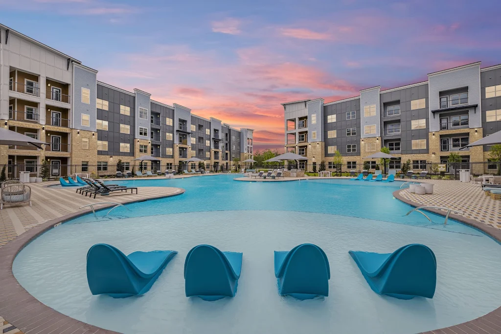 Resort-style swimming pool at dusk with large sundeck featuring lounge chairs, umbrellas, and seating