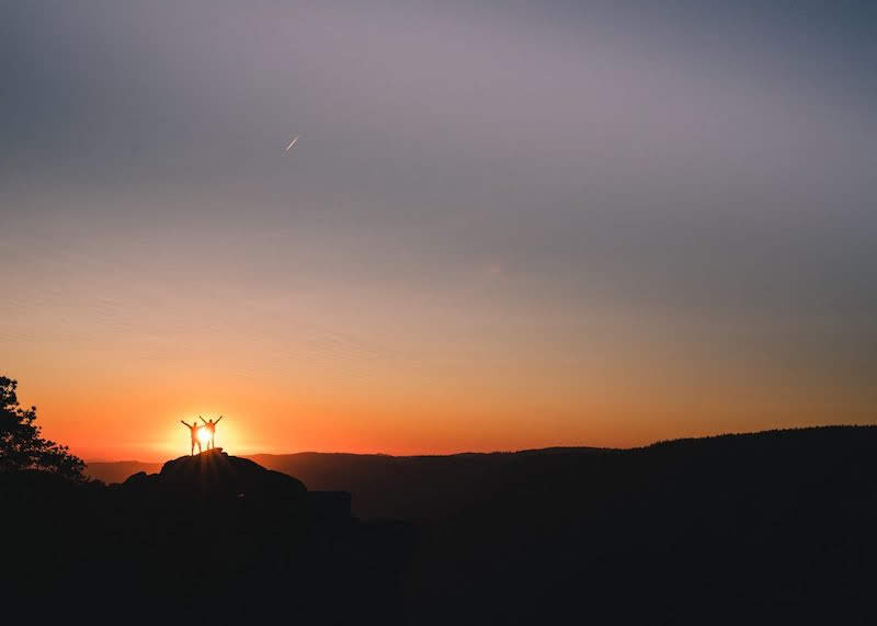 two people at the top of a summit against a sunset to encourage about how to achieve your goals