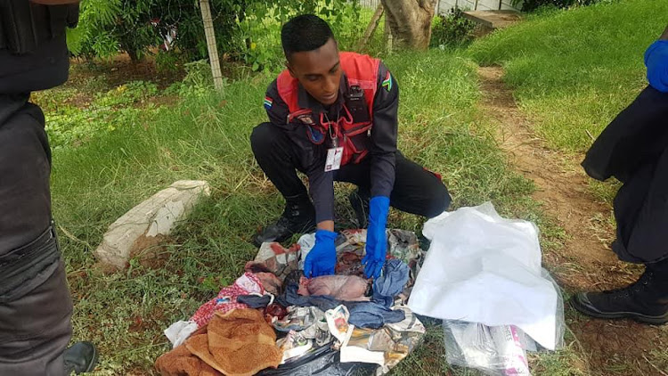 A paramedic reaches into a pile of refuse to take hold of a newborn baby boy who was dumped at the roadside in Verulam on Monday, January 14.