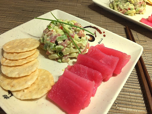 Slices of tuna on a plate with rice crackers and a slaw garnished with chives. 