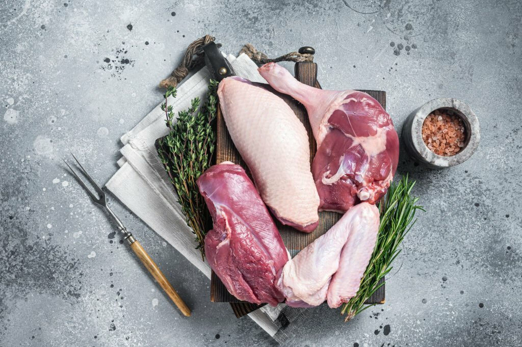 Butchered whole duck, raw breast steak, legs, wings on a butcher cutting board. Gray background. Top view.