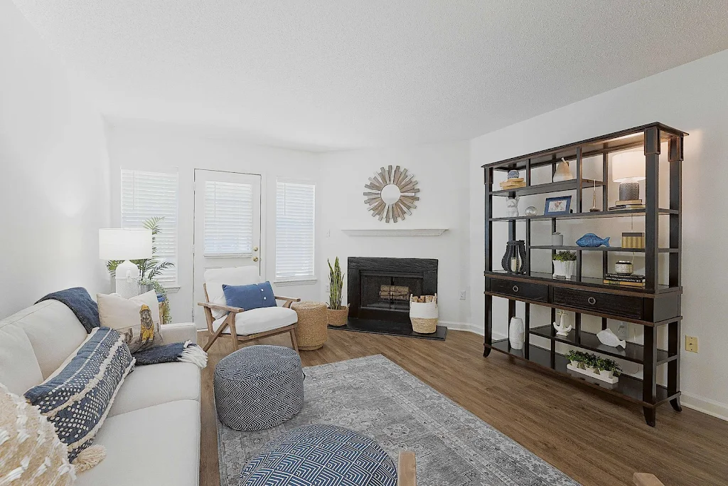 Model unit living room with plush couch and chair, wood-inspired flooring with a rug, fireplace, and decorative accents