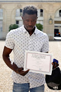 Mamoudou Gassama, 22, from Mali, displays a certificate of courage and dedication signed by Paris Police Prefect Michel Delpuech as he leaves the Elysee Palace after his meeting with French President Emmanuel Macron, in Paris, France, May 28, 2018.  