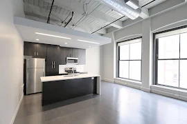 Open kitchen and living room with two large floor-to-ceiling windows, exposed ductwork, and plank flooring