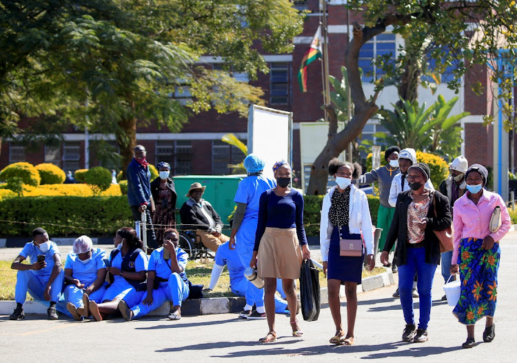 Poeple walk past Zimbabwean medical workers as they sit outside Sally Mugabe Hospital during a strike by state doctors and nurses to press for higher pay, in Harare, Zimbabwe, June 20, 2022.