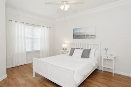 Furnished bedroom with ceiling fan, tan walls, and wood-inspired flooring