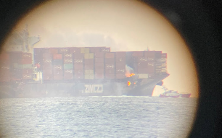 A fire is seen on the deck of the container ship ZIM Kingston in the waters off the coast of Victoria, British Columbia, Canada, October 23, 2021, as seen through a telescope, in this image obtained via social media.