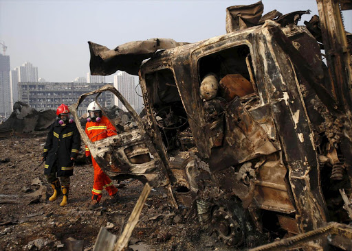 Firefighters walk past a damaged truck at the site of Wednesday night's explosions in Binhai new district of Tianjin, China, August 15, 2015