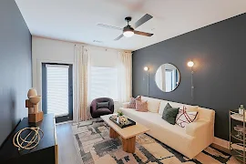 Model living room with dark accent walls, contemporary decor and furniture, patio door with blinds, and wood plank floors