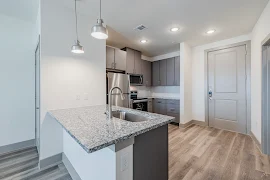 Apartment kitchen with stone countertops, stainless steel appliances, and sleek cabinetry in a bright space.