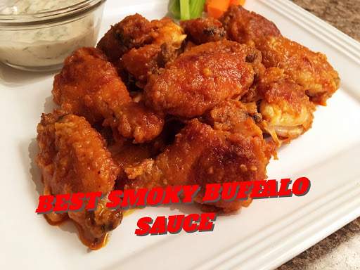 Chicken wings on a white plate with dipping sauce in a glass dish with veggies in the background.