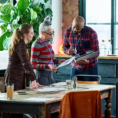 A man shares his laptop screen with two of his team members standing around a small conference table.