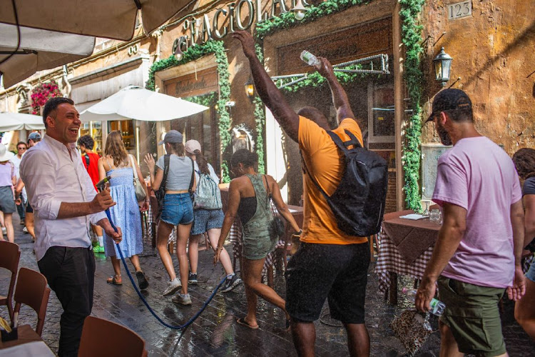 A restaurant employee sprays passersby with a water hose during hot weather caused by the Charon heat wave, in Rome, Italy, on Monday, July 17, 2023. The heat wave engulfing the Mediterranean is set to intensify as another Saharan anticyclone threatens record temperatures from Italy to Greece.