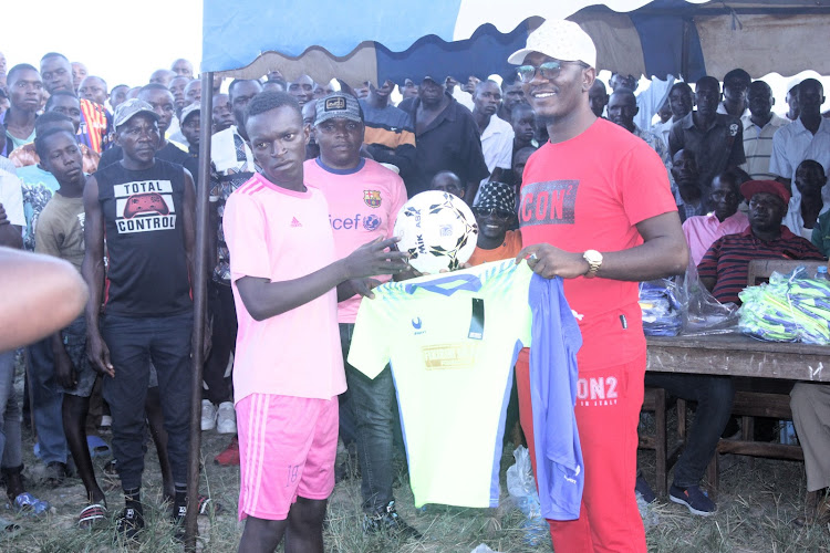 Kilifi county head of delivery unit in the office of the Governor Fikirini Jacobs awards a football jersey ball to the winning Kavunzoni team during the Mnagoni New Year party in Mitangano on Tuesday