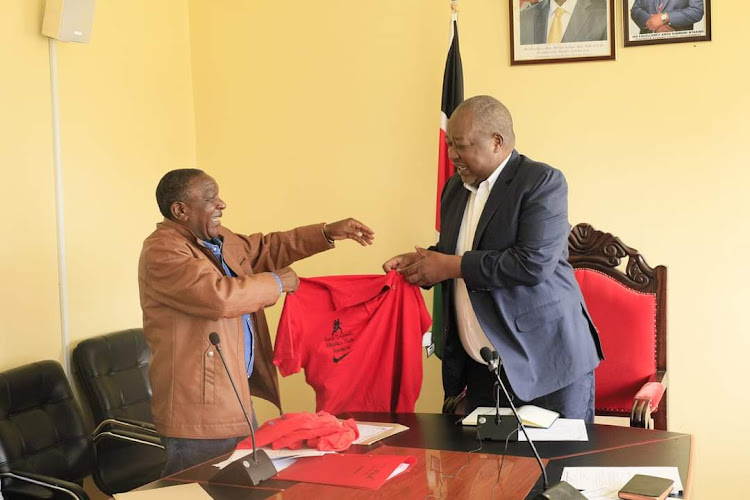 Gusii Sports Legends Welfare Association director Alfred Momanyi hands a tshirt to Nyamira Governor Amos Nyaribo