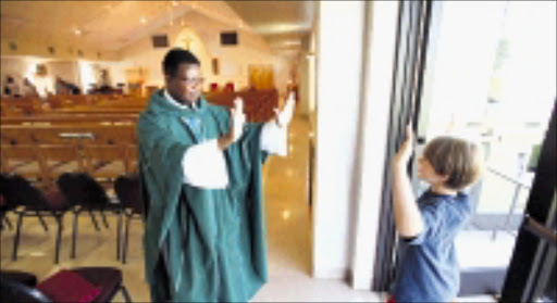 MINISTERING: The Reverend Chrispin Oneko greets a young parishioner in his Western Kentucky church. Pic. James Estrin. © The New York Times.