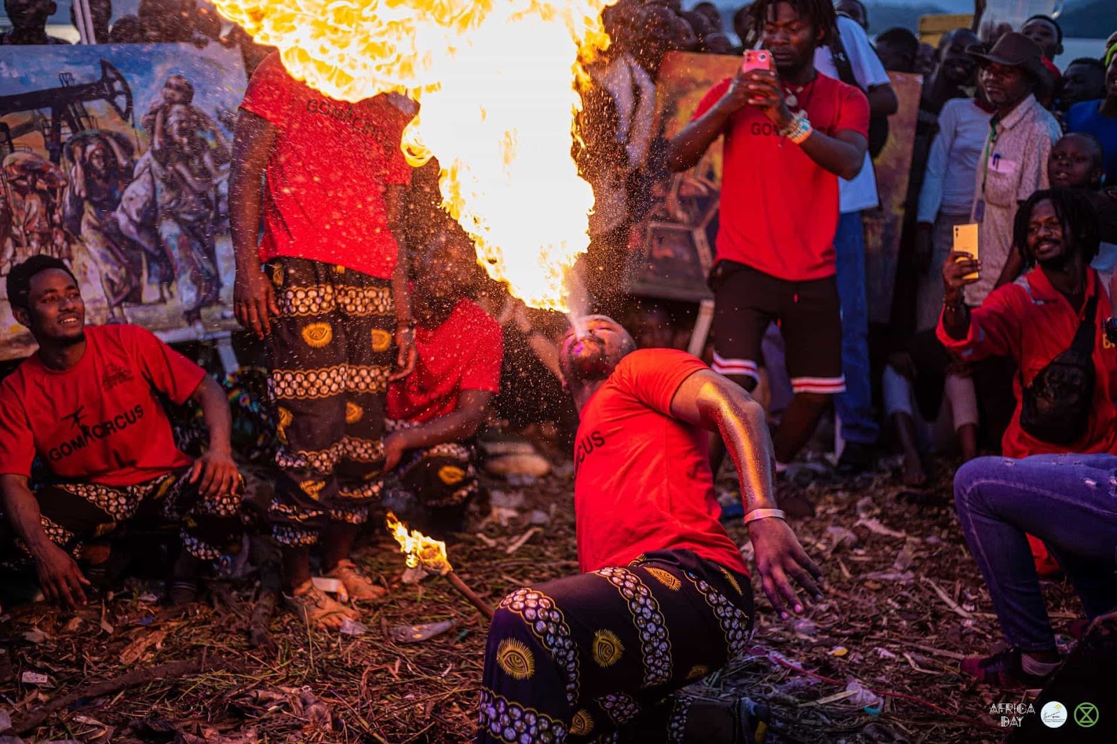 A crouching rebel breathes fire into the air as part of a performance in a market in DRC