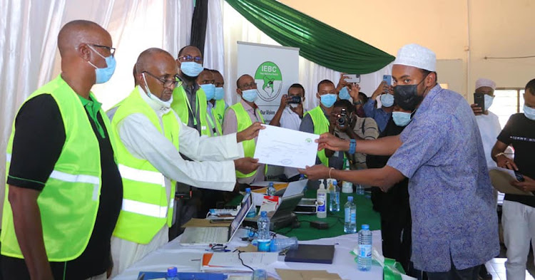 Garissa county returning officer Hussein Gure presents an IEBC nomination certificate to Abdikadir Mohamed Yussuf, son of the late Garissa Senator Yussuf Haji