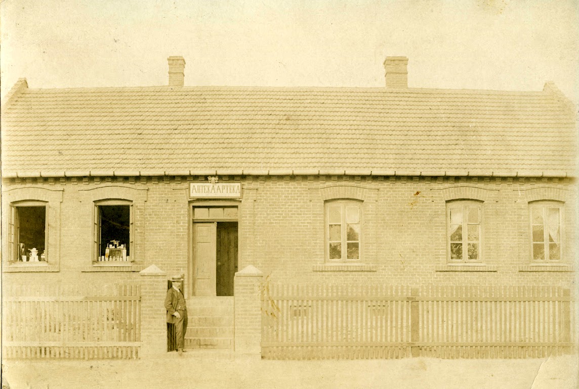 Zdjęcie: Apteka rodziny Zgrzebnickich w Chrobrzu. Zdjęcie wykonane na początku XX wieku (około 1910-15 roku). Przed apteką jej właściciel Józef Zgrzebnicki. Widać napis w języku polskim i rosyjskim. Budynek istnieje do dnia dzisiejszego przy ul. Staropolskiej (właścicielem jest Andrzej Sobota) budynek przylega bezpośrednio do działki należącej do parafii Chroberz.  (fot. z arch.Wiesława Grabik)