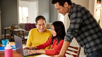 Una niña está sentada en la mesa, usando una Chromebook junto a dos adultos.