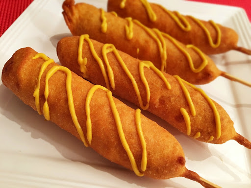 Four corn dogs with mustard on a white plate.