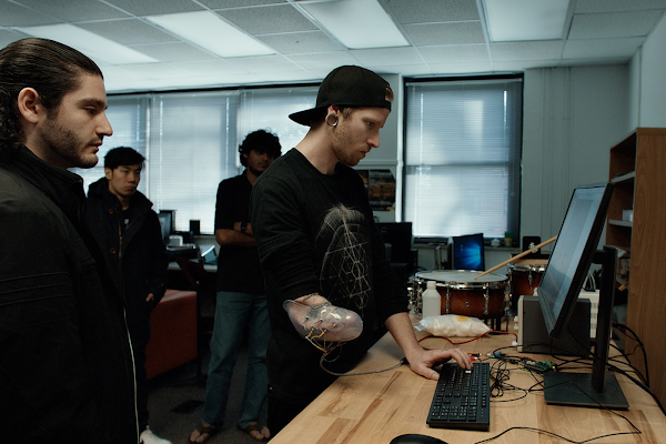 Jason Barnes in a classroom looking at a laptop. Georgia Tech engineers stand on either side of him.