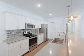 Kitchen with white cabinets, stainless steel appliances, grey countertops, grey tile backsplash, wood floors, pendant lights