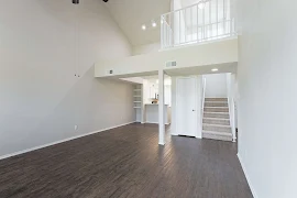 Living room with dark wood floors, vaulted ceilings, ceiling fan, carpeted stairs to second story