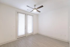 Living room with wood plank flooring, ceiling fan, and double glass door that leads to the patio. 