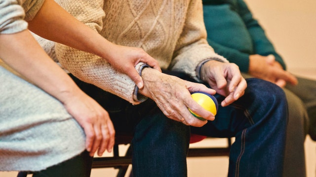 Compassionate carer helps elderly person to improve motor skills by squeezing a ball