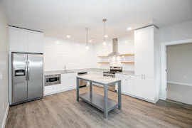 Kitchen with wood-inspired flooring, stainless steel appliances, white cabinets, and stone countertops