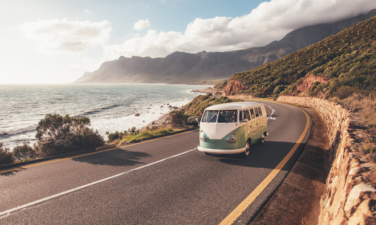 Group of friends traveling by a van on highway along the sea.